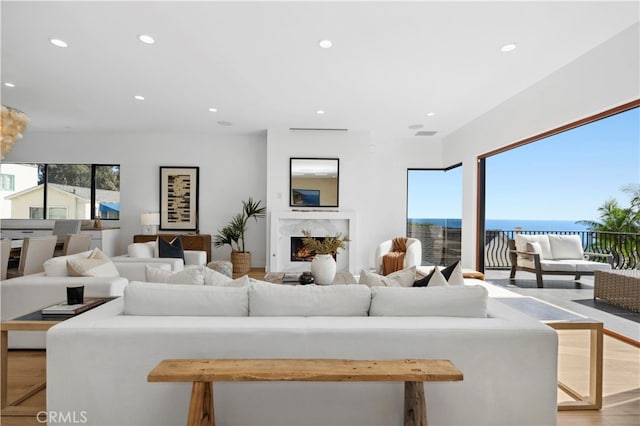 living room with light wood-type flooring, a water view, and a high end fireplace