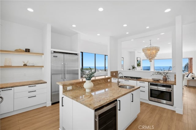 kitchen featuring an island with sink, white cabinets, wine cooler, and appliances with stainless steel finishes