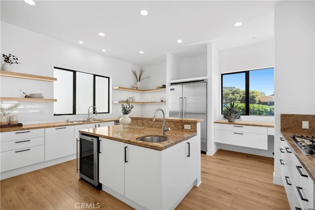 kitchen featuring wine cooler, light hardwood / wood-style floors, sink, white cabinets, and a center island with sink