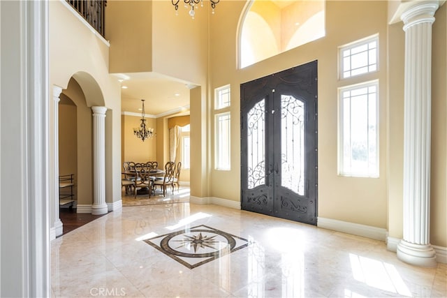 entrance foyer featuring french doors, a towering ceiling, decorative columns, crown molding, and a notable chandelier