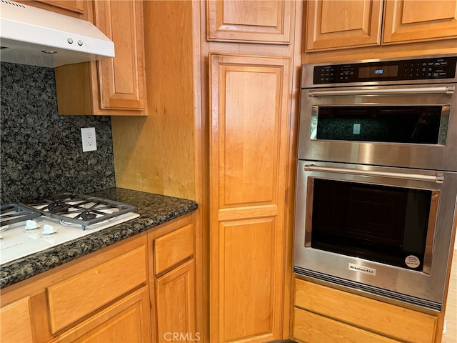 kitchen with stainless steel double oven, backsplash, dark stone countertops, and white gas stovetop