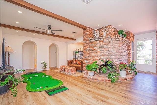 recreation room with hardwood / wood-style floors, ceiling fan, a fireplace, and beamed ceiling