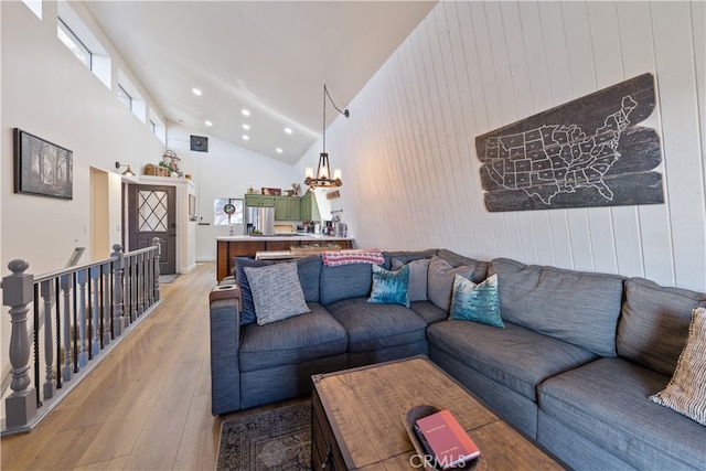 living room with high vaulted ceiling, light wood-type flooring, an inviting chandelier, and wooden walls