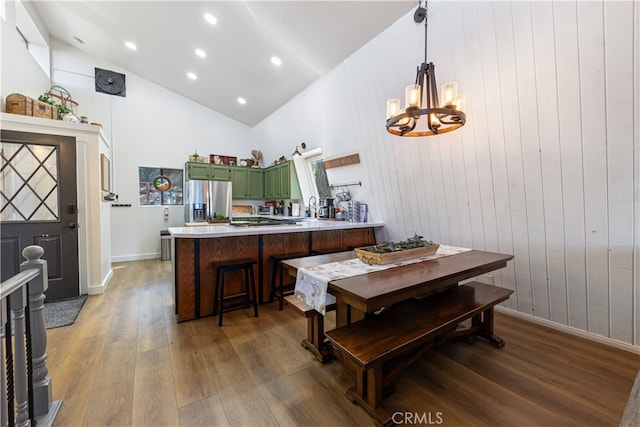 dining space featuring a chandelier, sink, high vaulted ceiling, wooden walls, and hardwood / wood-style floors