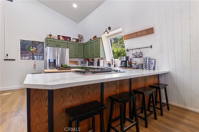 kitchen with appliances with stainless steel finishes, kitchen peninsula, green cabinetry, and light hardwood / wood-style flooring