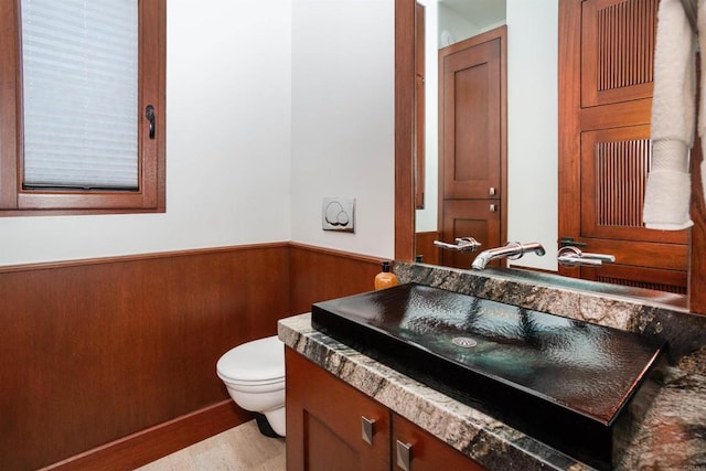 bathroom featuring toilet, wood walls, vanity, and hardwood / wood-style floors