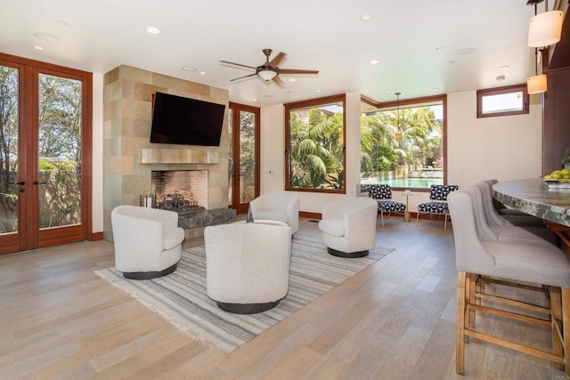 living room featuring light hardwood / wood-style floors, a wall of windows, a tile fireplace, and ceiling fan