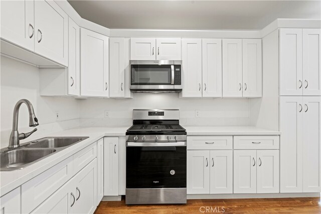 kitchen with stainless steel appliances, white cabinetry, light hardwood / wood-style floors, and sink