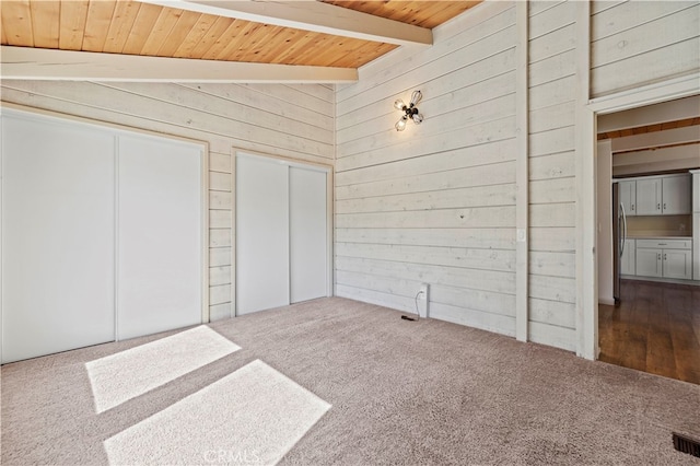 unfurnished bedroom featuring stainless steel fridge, wood walls, wooden ceiling, carpet flooring, and vaulted ceiling with beams