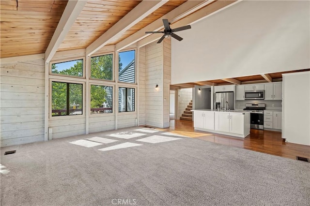 unfurnished living room featuring ceiling fan, beam ceiling, carpet floors, high vaulted ceiling, and stairs
