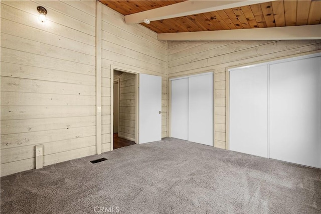 unfurnished bedroom with visible vents, wood walls, multiple closets, beam ceiling, and carpet flooring