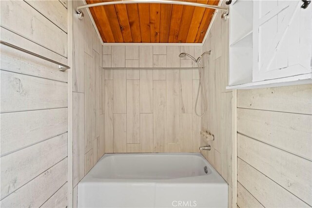 bathroom featuring wood ceiling, wooden walls, and tiled shower / bath