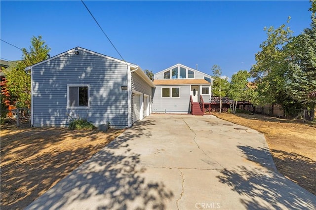 rear view of property featuring an attached garage, fence, and concrete driveway