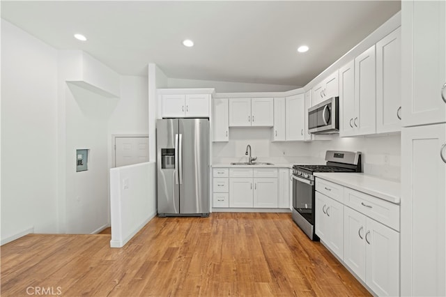 kitchen featuring lofted ceiling, sink, white cabinetry, stainless steel appliances, and light wood-type flooring