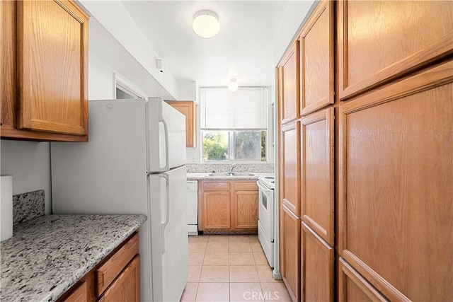 kitchen featuring light stone countertops, sink, light tile patterned floors, and white appliances