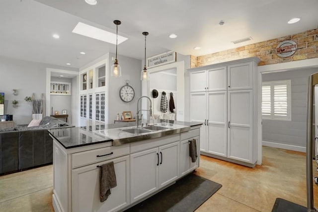 kitchen featuring a skylight, sink, an island with sink, hanging light fixtures, and white cabinets