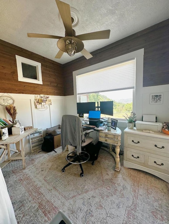 home office featuring wood walls, a textured ceiling, light colored carpet, and ceiling fan