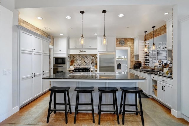 kitchen featuring a breakfast bar, an island with sink, built in appliances, and white cabinets