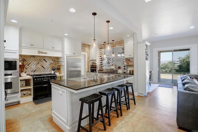 kitchen featuring white cabinets, tasteful backsplash, an island with sink, dark stone counters, and black appliances