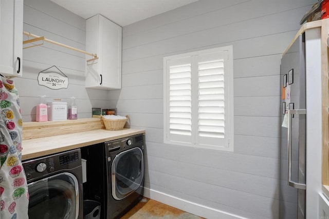 clothes washing area featuring wood walls, washer and dryer, and cabinets