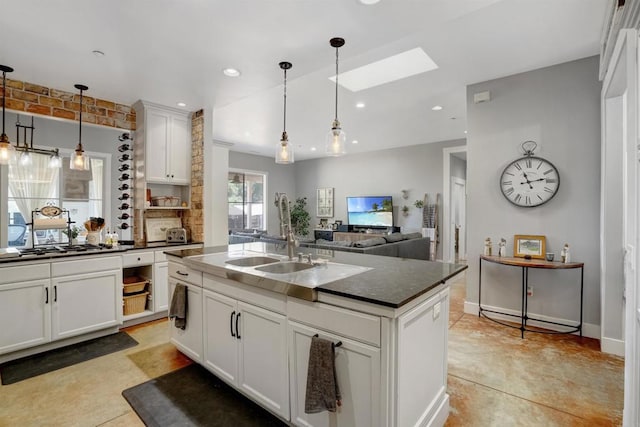 kitchen featuring a skylight, sink, an island with sink, white cabinetry, and pendant lighting