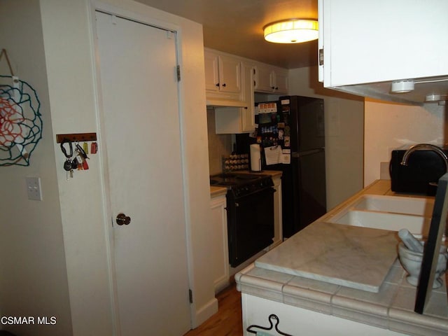 kitchen with custom range hood, black appliances, wood-type flooring, tile countertops, and white cabinets