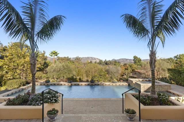 view of swimming pool with a water and mountain view and an in ground hot tub