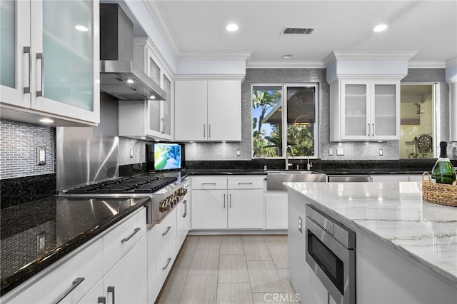 kitchen with sink, white cabinets, wall chimney range hood, stainless steel appliances, and dark stone countertops