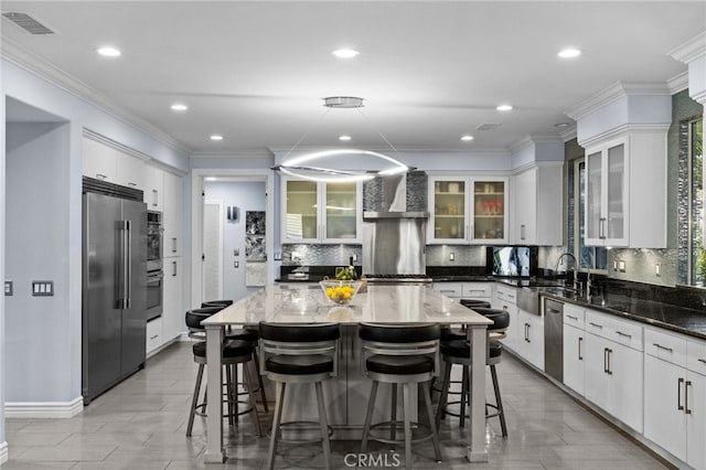 kitchen with white cabinets, stainless steel appliances, wall chimney exhaust hood, and a kitchen island