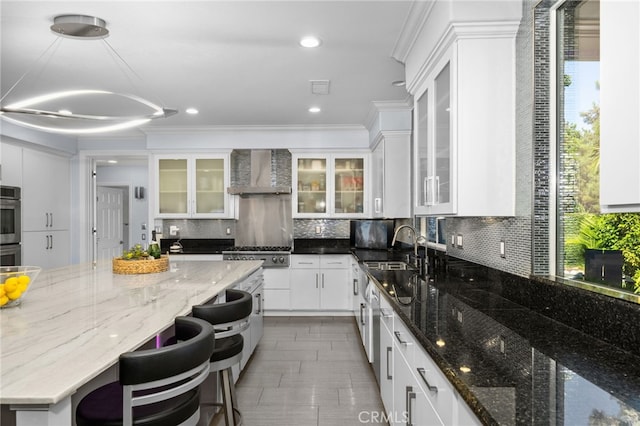 kitchen with dark stone counters, white cabinetry, decorative light fixtures, and wall chimney exhaust hood