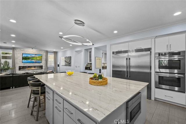 kitchen featuring a fireplace, a kitchen island, built in appliances, pendant lighting, and crown molding