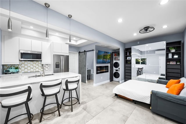 interior space featuring appliances with stainless steel finishes, white cabinets, a barn door, pendant lighting, and stacked washer and dryer