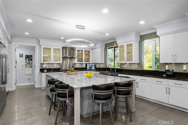 kitchen featuring white cabinets, pendant lighting, a kitchen island, wall chimney exhaust hood, and dark stone counters