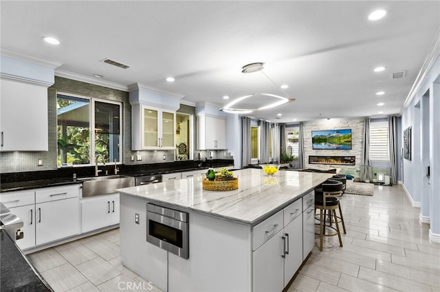 kitchen with a kitchen island, a fireplace, white cabinetry, and sink