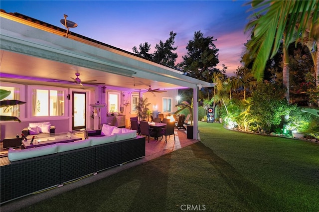 back house at dusk featuring a lawn, an outdoor hangout area, ceiling fan, and a patio area