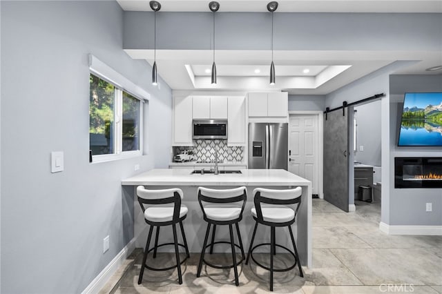 kitchen with hanging light fixtures, white cabinetry, a barn door, kitchen peninsula, and stainless steel appliances