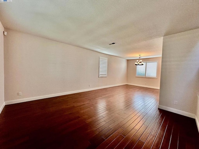 empty room featuring dark hardwood / wood-style flooring, a textured ceiling, and an inviting chandelier