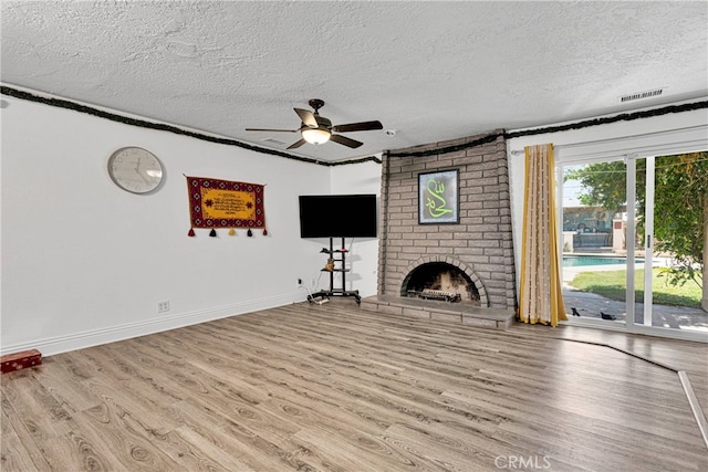 unfurnished living room featuring light wood-type flooring, a textured ceiling, ceiling fan, and a brick fireplace