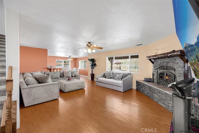 living room featuring a fireplace, hardwood / wood-style floors, a textured ceiling, and ceiling fan