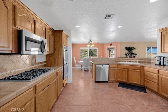 kitchen featuring ceiling fan, tile counters, sink, stainless steel appliances, and decorative backsplash