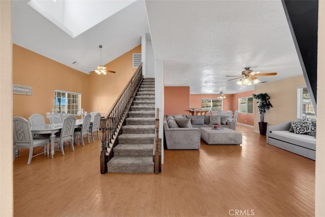 living room with ceiling fan, a towering ceiling, and light hardwood / wood-style floors