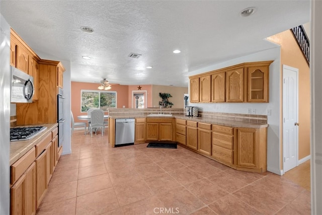 kitchen with ceiling fan, stainless steel appliances, kitchen peninsula, a textured ceiling, and light tile patterned floors