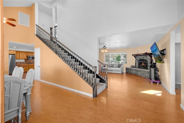 stairs featuring hardwood / wood-style floors, ceiling fan, a fireplace, and a high ceiling