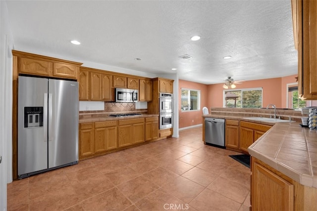 kitchen featuring tile counters, sink, stainless steel appliances, backsplash, and light tile patterned floors