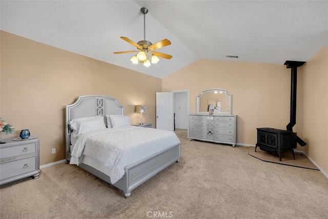 carpeted bedroom featuring vaulted ceiling, a wood stove, and ceiling fan