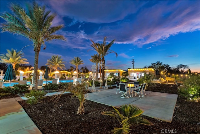 patio terrace at dusk featuring a community pool