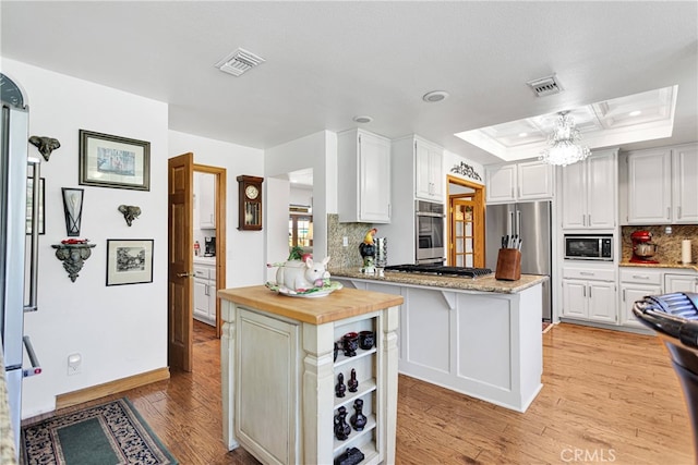 kitchen featuring light hardwood / wood-style flooring, white cabinets, a tray ceiling, and appliances with stainless steel finishes