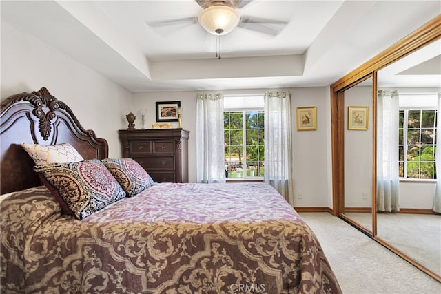 bedroom featuring a tray ceiling, light carpet, ceiling fan, and a closet