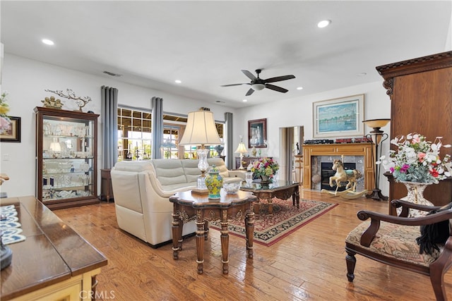 living room with wood-type flooring, a premium fireplace, and ceiling fan