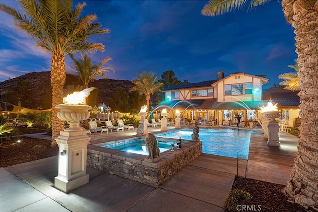 pool at dusk with pool water feature, a patio, and an in ground hot tub